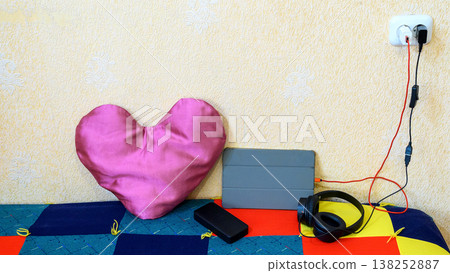 pink heart shaped pillow next to a tablet and headphones on a colorful background pink heart shaped pillow next to a tablet and headphones on a colorful background 138252887