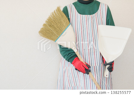 A woman in an apron holding a broom and dustpan. A woman in an apron holding a broom and dustpan. 138255577