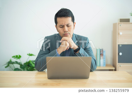 Thoughtful Businessman in Gray Suit Reflecting on Laptop Screen in Minimalist Office Environment with Natural Plants Background Thoughtful Businessman in Gray Suit Reflecting on Laptop Screen in Minimalist Office Environment with Natural Plants Background 138255979