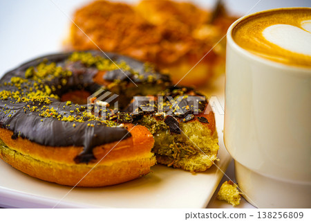 Dubai-style donuts with chocolate glaze topped with chopped pistachios, coffee 138256809