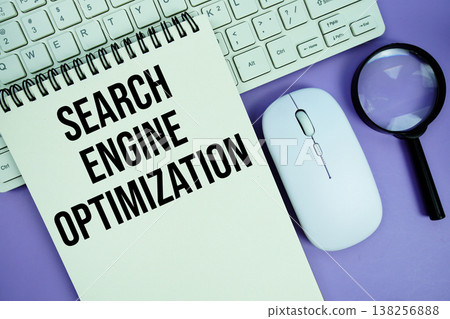 Notepad with the text "Search Engine Optimization" and white keyboard, wireless mouse, magnifying glass and alarm clock 138256888