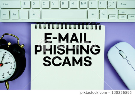 Notepad with the text "E-Mail Phishing Scams" with white keyboard, wireless mouse and alarm clock on purple background Notepad with the text "E-Mail Phishing Scams" with white keyboard, wireless mouse and alarm clock on purple background 138256895
