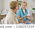 Conversation of smiling nurse and happy elderly patient in modern medical clinic 138257339