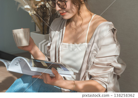 一位時尚的亞洲女性在家中客廳閱讀雜誌。 一位時尚的亞洲女性在家中客廳閱讀雜誌。 138258362