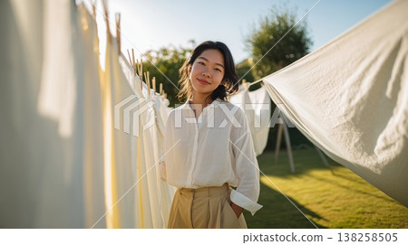 Young asian woman standing beside sunlit white laundry on a backyard clothesline at golden hour Young asian woman standing beside sunlit white laundry on a backyard clothesline at golden hour 138258505