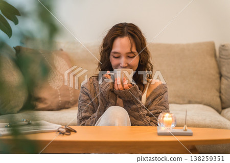 A stylish Asian woman sitting in her living room at night, sipping a hot drink. A stylish Asian woman sitting in her living room at night, sipping a hot drink. 138259351