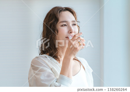 A woman drinking water from a cup in the living room to hydrate 138260264