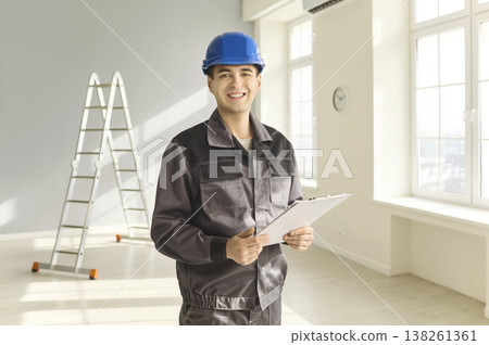 Smiling construction worker in helmet with clipboard in bright interior and ladder 138261361