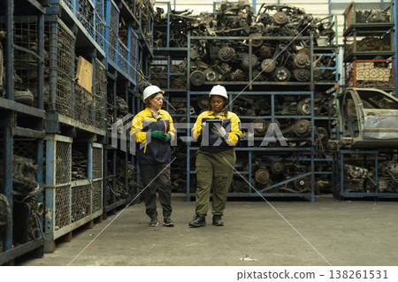 Hispanic female foreman and black female worker standing holding tablet, both of them checking inventory of auto parts and engine maintenance duties in factory. 138261531
