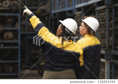 Hispanic female foreman and black female worker standing holding tablet, both of them checking inventory of auto parts and engine maintenance duties in factory. Hispanic female foreman and black female worker standing holding tablet, both of them checking inventory of auto parts and engine maintenance duties in factory. 138261544
