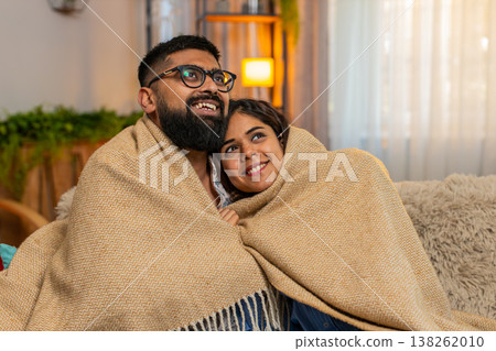 Indian family couple man woman cuddling under blanket at home, enjoying silence cozy peaceful moment Indian family couple man woman cuddling under blanket at home, enjoying silence cozy peaceful moment 138262010