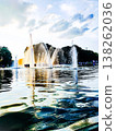 A fountain in the park sprays water into a calm pond with soft evening light. 138262036
