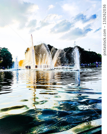 A fountain in the park sprays water into a calm pond with soft evening light. 138262036
