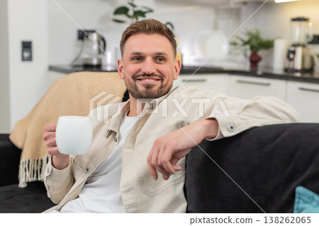 Young man enjoys herbal tea holds warm cup smiles breathes aroma takes pause and feels gentle relief Young man enjoys herbal tea holds warm cup smiles breathes aroma takes pause and feels gentle relief 138262065
