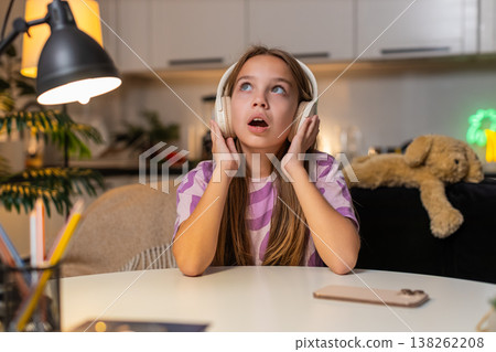 Teenager girl listens audiobook with wireless headphones focused smile surprise reacts to story joy Teenager girl listens audiobook with wireless headphones focused smile surprise reacts to story joy 138262208