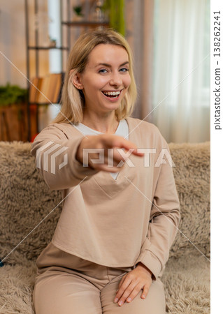 Adult woman pointing at camera and waving with joyful energy, smiling and playfully greeting at home Adult woman pointing at camera and waving with joyful energy, smiling and playfully greeting at home 138262241