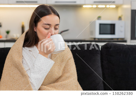 Young woman enjoys hot tea wrapped in blanket slow calm breath cozy rest warm cup gentle peace hush Young woman enjoys hot tea wrapped in blanket slow calm breath cozy rest warm cup gentle peace hush 138262380