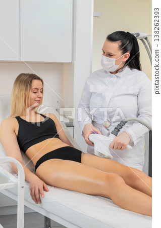 Woman receives cavitation vacuum massage on thighs in beauty clinic by professional cosmetologist Woman receives cavitation vacuum massage on thighs in beauty clinic by professional cosmetologist 138262393