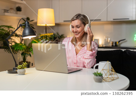 Adult woman in headphones tweaks layout on laptop moves layers nods to music smiles saves version Adult woman in headphones tweaks layout on laptop moves layers nods to music smiles saves version 138262395
