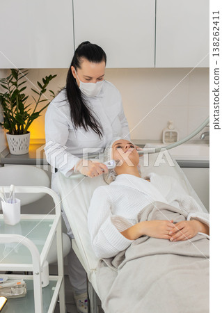 Woman receives RF lifting facial massage therapy by cosmetologist using professional equipment 138262411