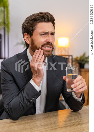 Middle-aged businessman drinks cold water winces tooth pain urgently searches dentist via smartphone Middle-aged businessman drinks cold water winces tooth pain urgently searches dentist via smartphone 138262655