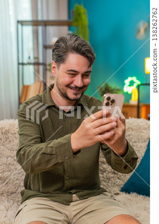 Middle-aged man happy smiling nodding reading smartphone message relaxing on home sofa couch indoors Middle-aged man happy smiling nodding reading smartphone message relaxing on home sofa couch indoors 138262762