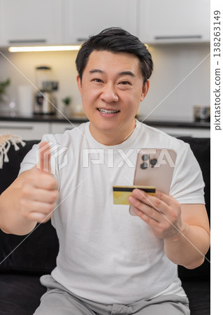 Asian man completes payment with smartphone and credit card smiles at confirmation shows thumbs up 138263149