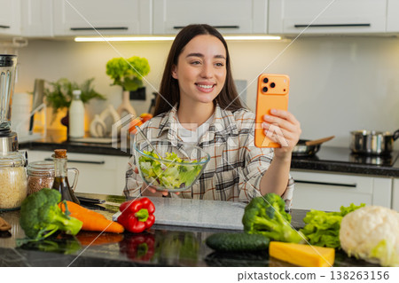 Young woman vlogger films healthy keto cooking tips presenting vegetable salad to followers on phone 138263156