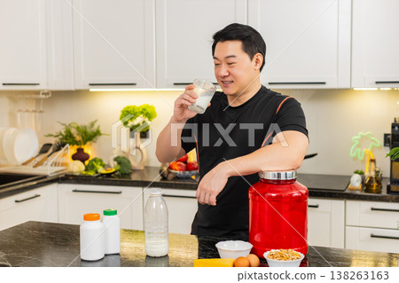 Asian man in kitchen pours glass of milk and drinks protein rich drink for healthy muscle growth fit Asian man in kitchen pours glass of milk and drinks protein rich drink for healthy muscle growth fit 138263163