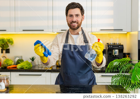 Middle-aged man smiling while cleaning kitchen table with cloth for home hygiene and freshness daily Middle-aged man smiling while cleaning kitchen table with cloth for home hygiene and freshness daily 138263292