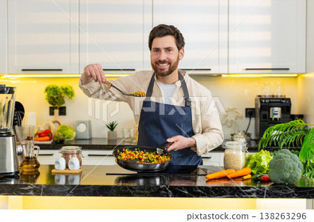 Middle-aged man tasting vegetables on skillet pan at home kitchen cooking healthy diet meal on stove Middle-aged man tasting vegetables on skillet pan at home kitchen cooking healthy diet meal on stove 138263296