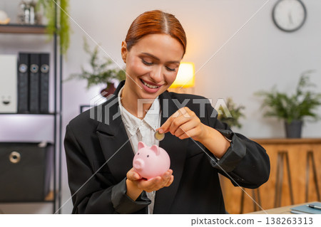 Young businesswoman drops coins into piggy bank planning future savings wealth growth security goal Young businesswoman drops coins into piggy bank planning future savings wealth growth security goal 138263313