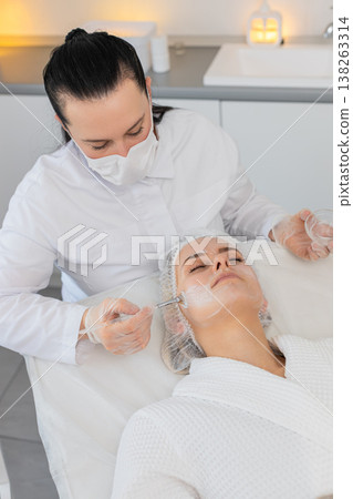 Enzyme therapy, beautician applying moisturizing medical cream on young woman face with brushes 138263314