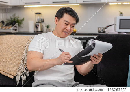 Asian man reviews contract reads fine print and signs with confident steady hand after careful check Asian man reviews contract reads fine print and signs with confident steady hand after careful check 138263351
