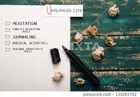 Notebook with checklist for balanced life, featuring meditation, journaling, physical activities, and productivity skills, surrounded by crumpled paper and a black pen on a wooden table 138265702