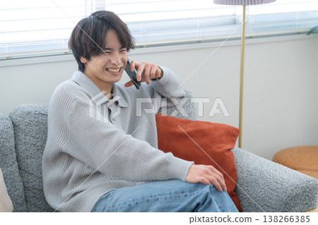 A young man is looking at his smartphone by the living room window. A young man is looking at his smartphone by the living room window. 138266385
