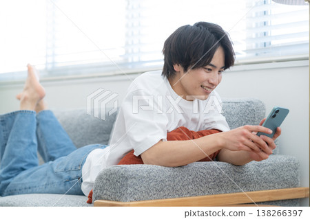 A young man is looking at his smartphone by the living room window. A young man is looking at his smartphone by the living room window. 138266397