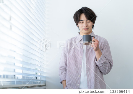 一位年輕男子在客廳窗邊放鬆休息。 138266414