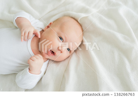 Happy baby. Cute little newborn girl with smiling face lying on bed in bedroom. Infant baby resting playing lying down on white blanket at home. Motherhood happy child childcare concept Happy baby. Cute little newborn girl with smiling face lying on bed in bedroom. Infant baby resting playing lying down on white blanket at home. Motherhood happy child childcare concept 138266763