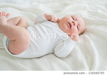 Happy baby. Cute little newborn girl with smiling face lying on bed in bedroom. Infant baby resting playing lying down on white blanket at home. Motherhood happy child childcare concept 138266785