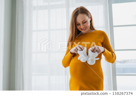 Pregnancy motherhood people expectation future. Pregnant woman with big belly holding newborn baby booties smiling at home. Young mom enjoying pregnancy. Maternity tenderness parenthood new life Pregnancy motherhood people expectation future. Pregnant woman with big belly holding newborn baby booties smiling at home. Young mom enjoying pregnancy. Maternity tenderness parenthood new life 138267374