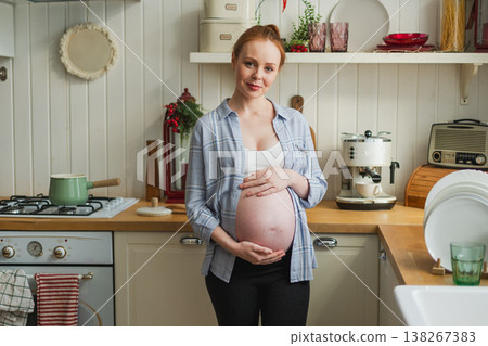 Pregnancy motherhood people expectation future. Pregnant woman with big belly smiling in kitchen at home. Girl hugging her tummy enjoying pregnancy. Maternity tenderness parenthood new life concept 138267383