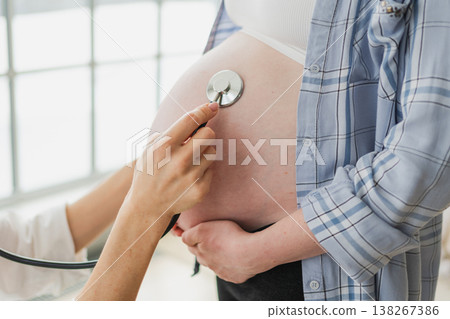 Doctor examining pregnant woman holding stethoscope near big belly listening baby heartbeat. Gynecologist doctor consulting patient about pregnancy in hospital office. Visit to doctor medical checkup Doctor examining pregnant woman holding stethoscope near big belly listening baby heartbeat. Gynecologist doctor consulting patient about pregnancy in hospital office. Visit to doctor medical checkup 138267386