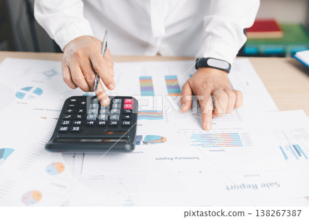 Business analyst calculating figures on calculator and pointing at summary report charts, reviewing financial data for budgeting, accounting, audit, taxation, KPI tracking and forecasting decisions. Business analyst calculating figures on calculator and pointing at summary report charts, reviewing financial data for budgeting, accounting, audit, taxation, KPI tracking and forecasting decisions. 138267387