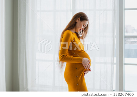 Pregnancy motherhood people expectation future. Pregnant woman with big belly standing near window at home. Girl hugging her tummy enjoying pregnancy. Maternity tenderness parenthood new life concept 138267400