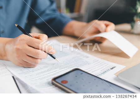 Tax preparation with hand signing tax form using pen, holding receipt, smartphone calculator app on desk, illustrating income return filing, deductions, compliance and audit review. tax, preparation Tax preparation with hand signing tax form using pen, holding receipt, smartphone calculator app on desk, illustrating income return filing, deductions, compliance and audit review. tax, preparation 138267434