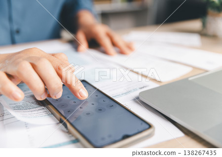 Tax preparation with hand signing a tax form using pen, holding receipt, smartphone calculator app on desk, illustrating income return filing, deductions, compliance and audit review. tax, preparation 138267435