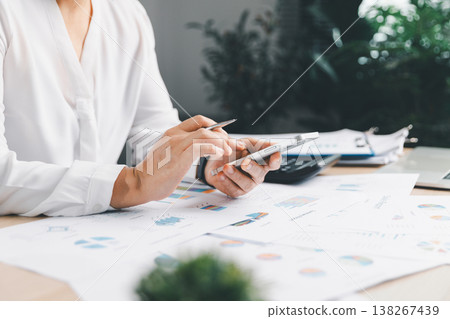 Business analyst checking financial charts and reports while using smartphone and pen at office desk, reviewing data for budgeting, accounting, KPI tracking, forecasting and planning. analyst data Business analyst checking financial charts and reports while using smartphone and pen at office desk, reviewing data for budgeting, accounting, KPI tracking, forecasting and planning. analyst data 138267439
