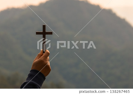 Hand holding wooden cross in front of misty mountain at sunrise, symbol of Christian faith, prayer, worship and hope. Spiritual background with copy space for inspirational design. spiritual Christian Hand holding wooden cross in front of misty mountain at sunrise, symbol of Christian faith, prayer, worship and hope. Spiritual background with copy space for inspirational design. spiritual Christian 138267465