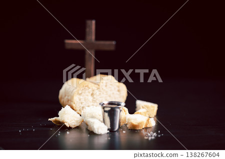 Still life of communion bread and silver cup of red wine with wooden cross on dark table, symbolizing Christian Eucharist, worship, faith, sacrifice and remembrance with copy space. Still life of communion bread and silver cup of red wine with wooden cross on dark table, symbolizing Christian Eucharist, worship, faith, sacrifice and remembrance with copy space. 138267604